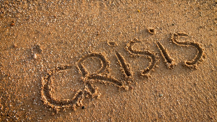 Closeup image of word Crisis written on the wet sand at beach