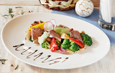 Dish of meat and vegetables on a white plate on a wooden table