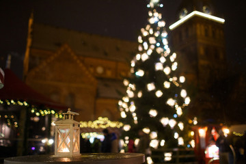 a lantern with a candle on the background of a city fair and a Christmas tree with lights