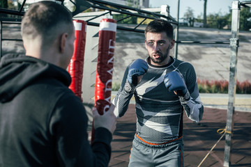 Serious boxer looking at the trainer while mastering his punches