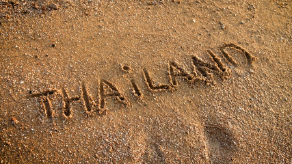 Closeup photo of word Thailand written on sea beach with golden sand. Concept of tourism, traveling, trips and journeys in Asia.