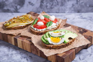 Beautiful healthy snack - sandwiches with rye bread with avocado and egg, mozzarella and tomato, cream cheese and pear. Healthy vegetarian food concept
