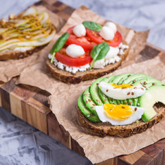 Beautiful healthy snack - sandwiches with rye bread with avocado and egg, mozzarella and tomato, cream cheese and pear. Healthy vegetarian food concept