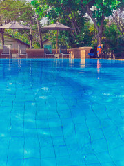 Sun beds are under umbrellas around the pool. The pool is filled with clean water. Tropical plants can be seen behind.