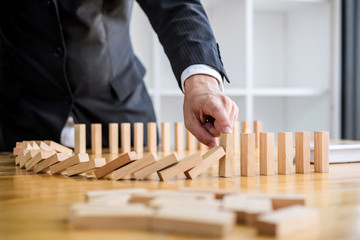 Wooden game strategy, Businessman hand stopping falling wooden dominoes effect from continuous...