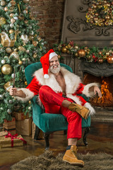 Angry Bad Santa Claus, is in the Christmas room with a fireplace and a Christmas tree, sitting in a...