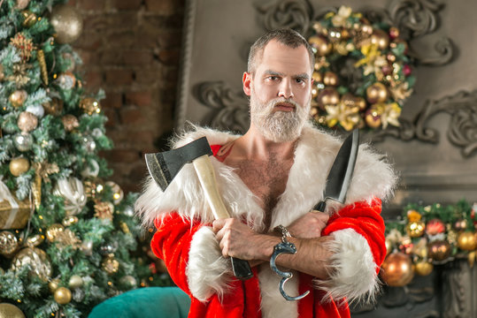 Portrait of an evil bad Santa Claus with an ax and a knife on the background of the Christmas tree