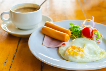 Fototapeta premium Fried egg with sausage and ham served with vegetable salad and hot coffee for appetizing breakfast.