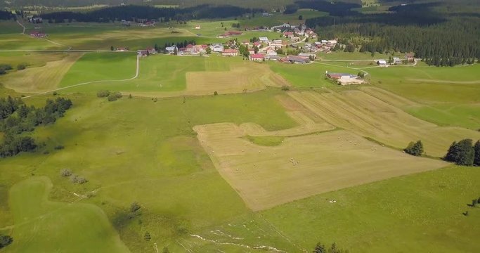 Aerial, tilt up, drone shot, over green fields, with a view of a small town in the french countryside, in Chapelle des bois, Doubs and Jura regional park, Franche comt&radic;&copy;, in France