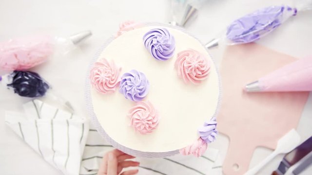 Flat lay. Piping pastel color buttercream rosettes on a white cake to make a unicorn cake.