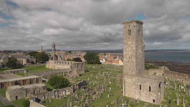 Aerial drone flying by one of the towers of the St Andrews Cathedral as other towers and the coastline come into view in the background in St Andrews, Scotland, UK. 4K footage shot on Mavic Air.