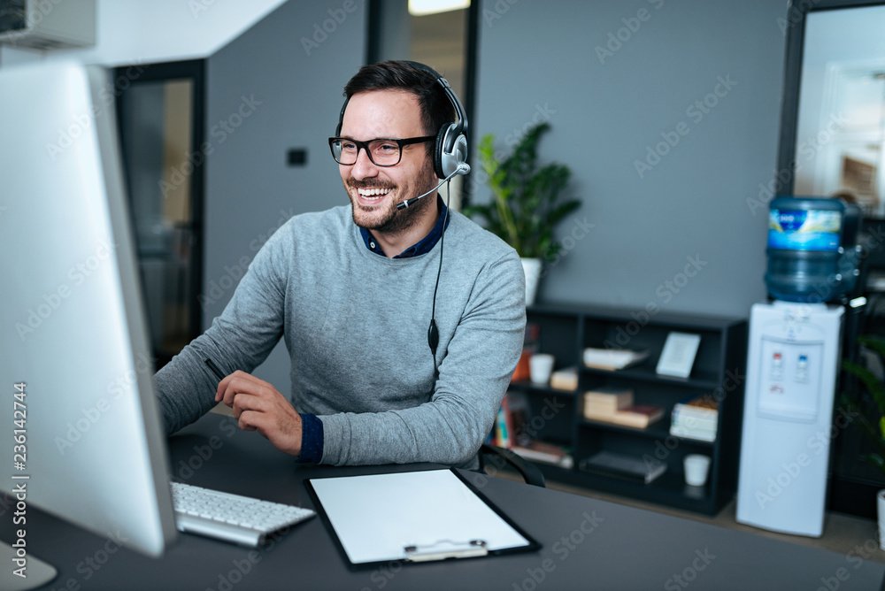 Wall mural Portrait of a handsome smiling man with headset working on the computer.