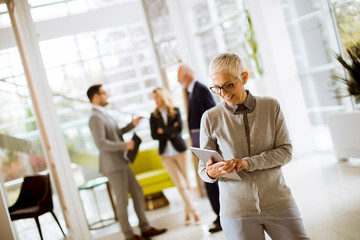 Portrait of senior businesswoman with digital tablet while other business people standing in background
