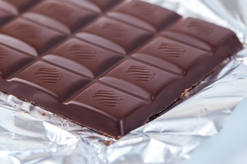 Dark chocolate bar in opened silver foil. Sweet food