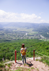 Fototapeta na wymiar Girl with a yellow backpack looking at a beautiful view from the mountain