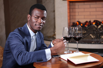 Young businessman African American in the restaurant on the background of the fireplace. Writing in...