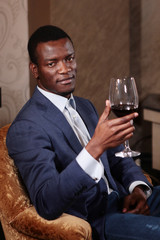 Portrait of an African American businessman with a glass of wine in his hand. Young businessman in a suit and in the interior of the restaurant. The concept of business travelers.