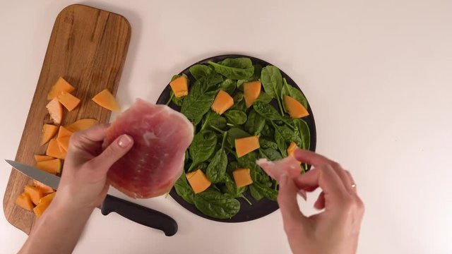 Fresh salad with spinach and figs and jamon and watermelon and blue cheese - putting jamon on black stone plate with watermelon on black stone plate and spinach on white background