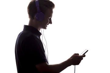 silhouette of a young man profile listening music in headphones, guy enjoying his favorite song on a white isolated background