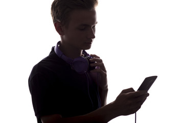 silhouette of ateenager boy with headphones on his neck,a guy flipping through a playlist of music on his electronic device on white isolated background
