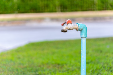 Old and weathered garden's faucet water tap in beautiful sunlight with green grass in background.