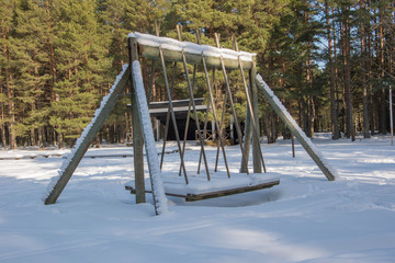 Big swing covered with snow on a sunny winter day in forest.
