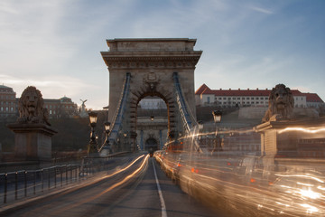  Langzeitbelichtung bei Sonnenschein. Autos fahren schnell über die Kettenbrücke am Ufer der Donau in Budapest, der Hauptstadt von Ungarn, Osteuropa