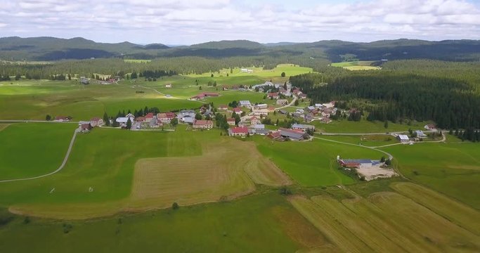 Aerial, tilt down, drone shot, flying over green fields, towards a small town in the french countryside, in Chapelle des bois, Doubs and Jura regional park, Franche comt&radic;&copy;, in France