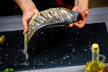 Chef hands cooking fresh fish carp with seasoning for baking on a shale board. flat top view, copy text menu