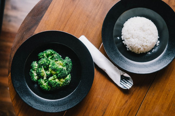Steamed plain rice and broccoli on two black plates from above. Creative minimalism, dark food photography, healthy eating concept