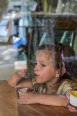  Little charming baby girl eating ice cream in a cafe, view through the window