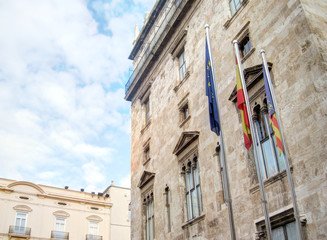 A landscape of the historical Valencin Community Palace (Palau de la Generalitat)  with European, Spanish and Valencian flags, in Valencia, Spain