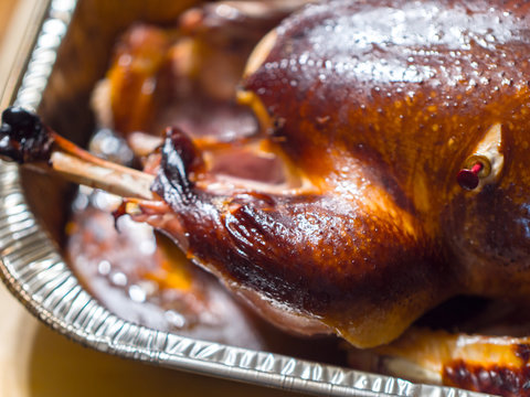 A closeup photograph of a grilled smoked turkey focusing on the leg with bone sticking out in a metal baking pan.