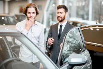 Car salesman helping a young ashamed client to make a decision showing intrerior of a luxury car at...
