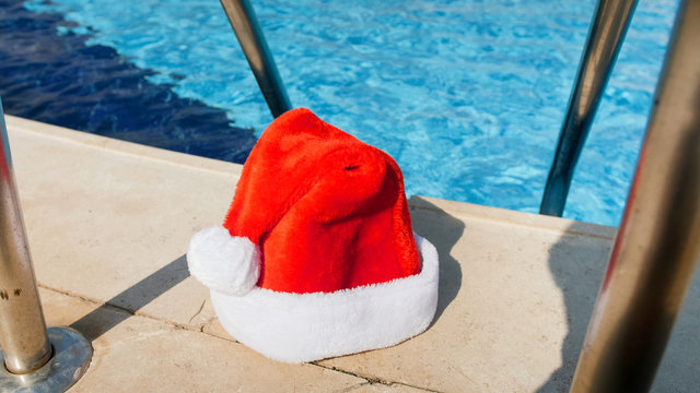 Image of Santa Claus left his hat outdoor swimming pool. Concept of travel and tourism on Christmas, New Year and winter holidays.