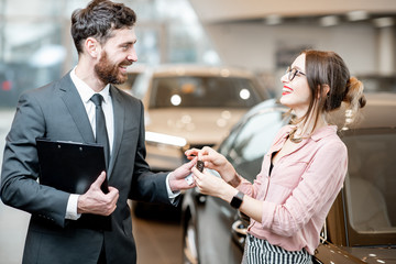Fototapeta premium Salesperson giving keys to a young happy woman in the showroom with luxury cars