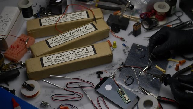 THE HANDS OF A TERRORIST CONSTRUCT A HIGH EXPLOSIVE BOMB.  4K OVERHEAD SLIDER SHOT.