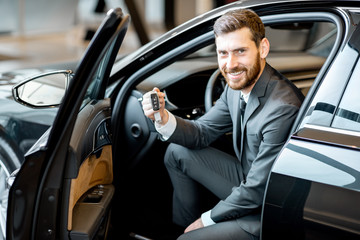 Portrait of a handsome businessman holding keys of a luxury car in the showroom