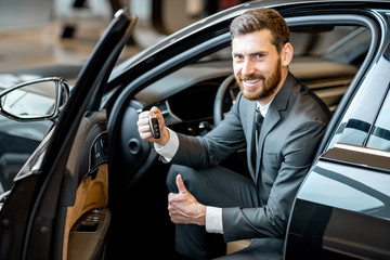 Portrait of a handsome businessman holding keys of a luxury car in the showroom