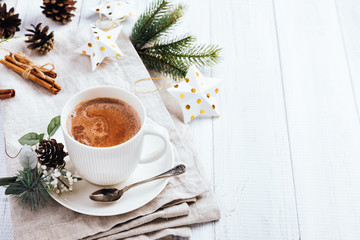 Cup of hot chocolate with cinnamon sticks on the white wooden table. Winter cocoa drink on a napkin, Christmas-tree golden stars decorations, branches and cones
