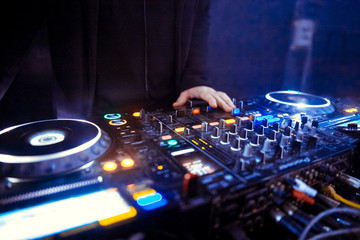 Hands of a DJ mixing music at a disco or concert with one hand on the switches and one held near...