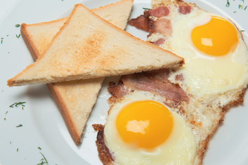 Appetizing fried eggs on white plate with toasts and bacon decorated with greenery. Nutritious breakfast. 