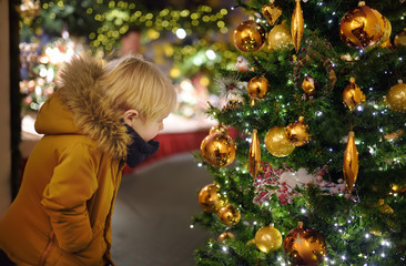 Little boy near Christmas tree decorating golden balls outdoors