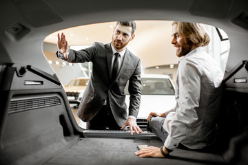 Salesman showing spacious trunk of a new car for a young man client in the showroom