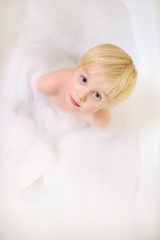 Cute little boy taking a foam bubble bath view from above