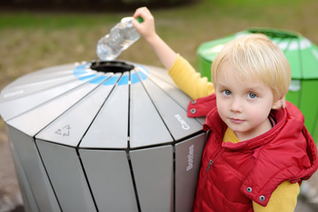 Little boy puts a plastic bottle in trash can for separate recycling.