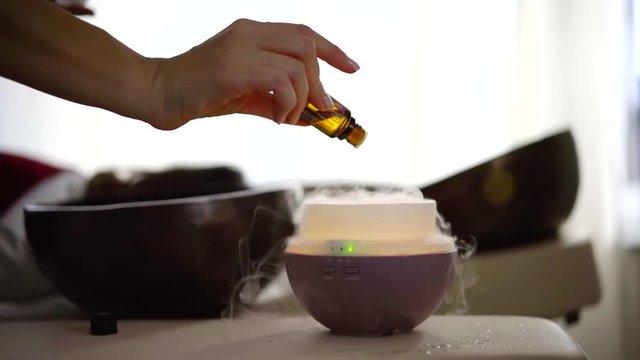 female hand is holding vial with essential oil and dropping it on aroma lamp, close-up view