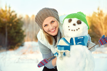 happy woman playing with snowman in the winter outdoors
