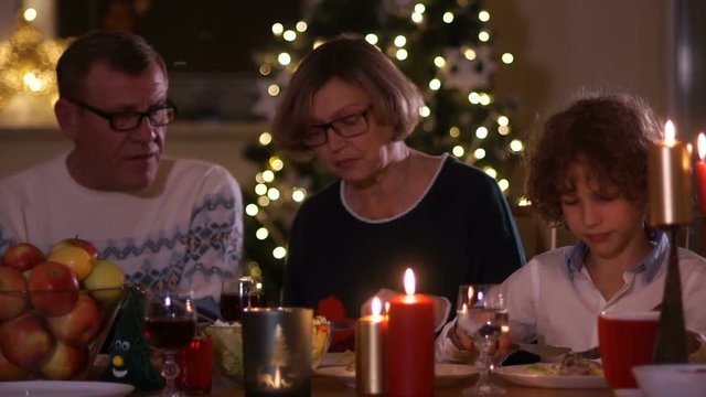 Grandfather and grandmother are talking to their grandson while sitting at a festive New Year's table. Candlelight dinner, happy family