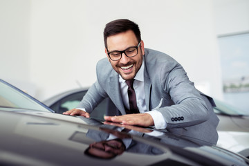 Fototapeta na wymiar Happy businessman touching car in auto show or salon
